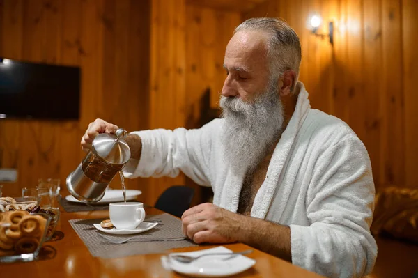 Человек наливает чай во время отдыха в сауне — стоковое фото