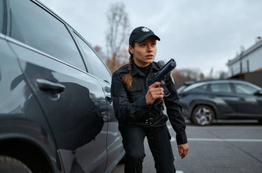Police woman aiming gun standing near car