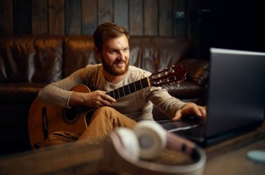 Gitar çalan adam dizüstü bilgisayara bakıyor.