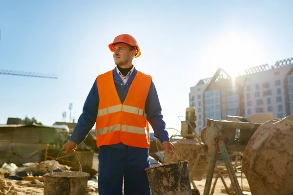 Budowniczy trzyma wiadro nad tłem placu budowy — Zdjęcie stockowe