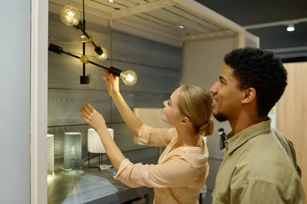 Smiling couple customers choosing lamp in store — Stock Photo, Image