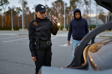 Kadın polis memuru el feneriyle arabayı inceliyor.