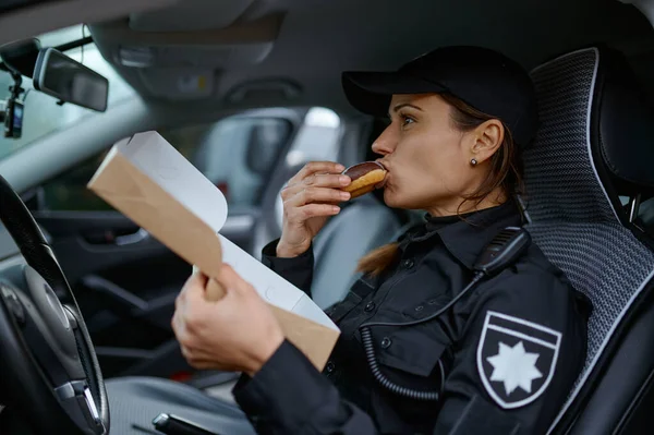 Donna agente di polizia mangiare ciambella in auto — Foto Stock