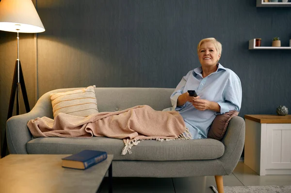 Зрелая женщина, завернутая в одеяло и смотрящая телевизор — стоковое фото