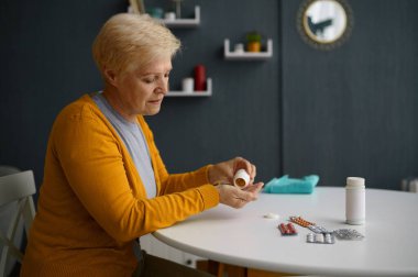 Elinde ilaç tutan beyaz saçlı, olgun bir kadın.