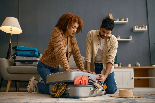 Couple trying to pack belongings into suitcase