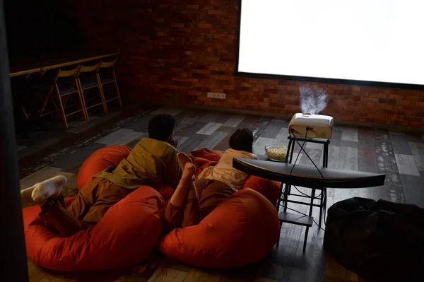 Para leżąca na miękkiej torbie oglądająca projektor — Zdjęcie stockowe