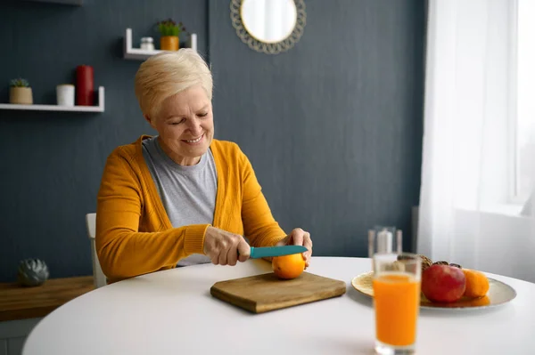 Пожилая женщина режет фрукты для свежего сока — стоковое фото