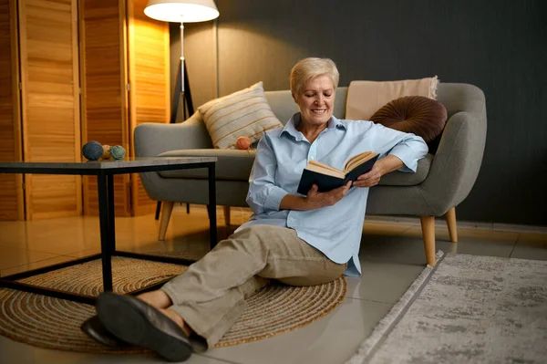 Старуха читает книгу сидя на диване — стоковое фото