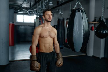 Kaslı erkek boksörün portresi boks arka planında ağır çantanın yanında duruyor.