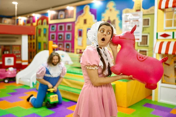 Portrait of woman like little baby playing with inflatable rubber pony for jumping on playroom background