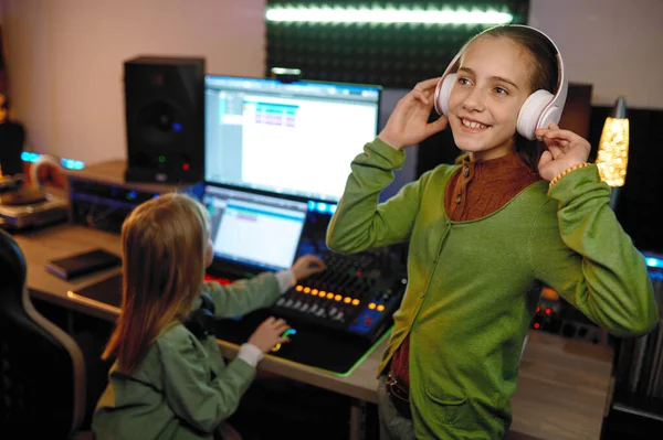 录音室的孩子们 把注意力集中在用无线耳机听音乐的年轻女孩的声音制作上 — 图库照片