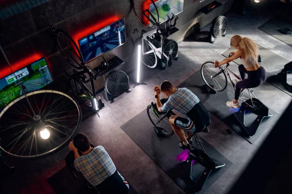 Group of sports people riding stationary bike exercise machine at gym. Fitness training indoor. Overhead view