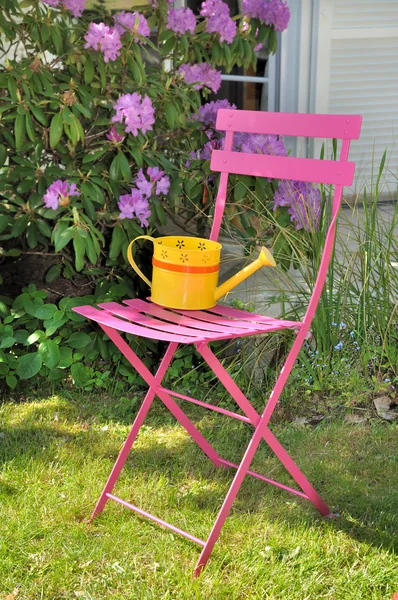 Decorative watering can on a chair i a garden — Stock Photo, Image