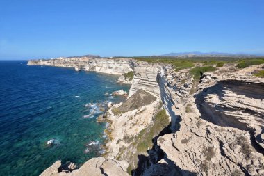 Bonifacio kıyıları, açık mavi gökyüzünde denize bakan kireçtaşı kayalıkları.