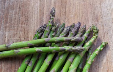 Ahşap masaya konmuş yeşil kuşkonmaz yığını. 