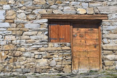 facade of old alpine chalet in stone with wooden door and shutters closed 
