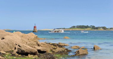 İngiltere, Benoit 'te tekneler ve deniz feneri arka planıyla kayalık sahil manzarası.