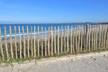  Britanya 'da mavi denizin ve gökyüzünün önündeki kumulda ahşap çit - Fransa