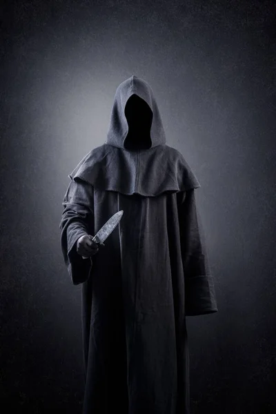 Hooded man with old knife in the dark