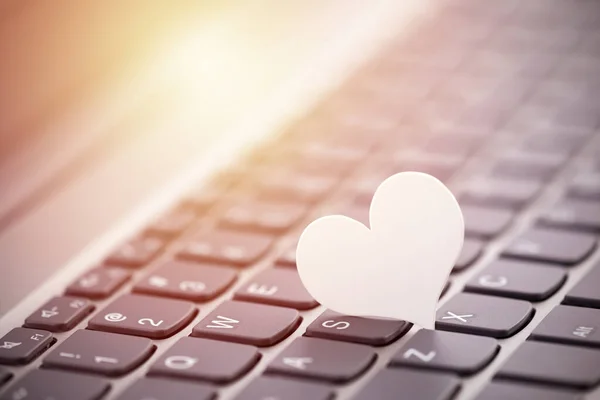 Small white paper heart on computer keyboard. Internet dating concept.
