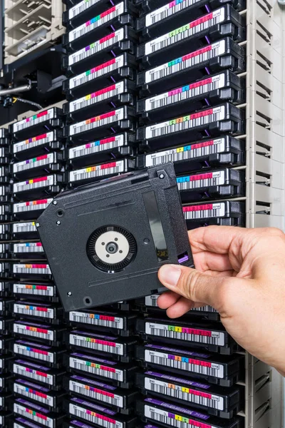 hand of a technician holding data storage magnetic tape in front of data storage array