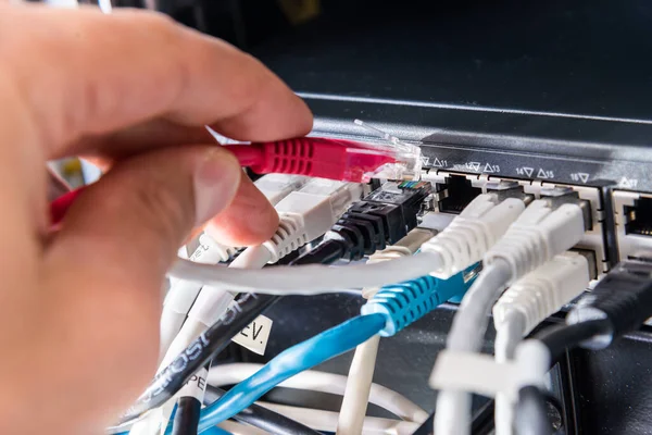 Hand of computer technician connecting fiber optics cable into data switch