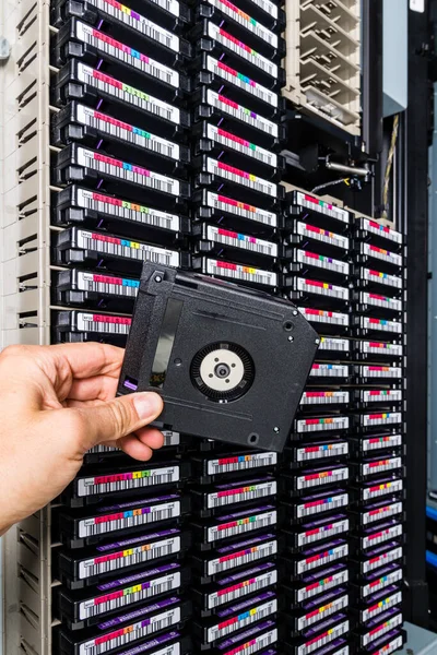 hand of a technician holding data storage magnetic tape in front of data storage array