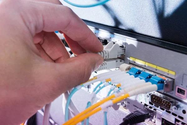 Hand of computer technician connecting fiber optics cable into data switch