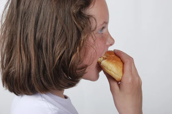 En ung flicka äter en bulle — Stockfoto
