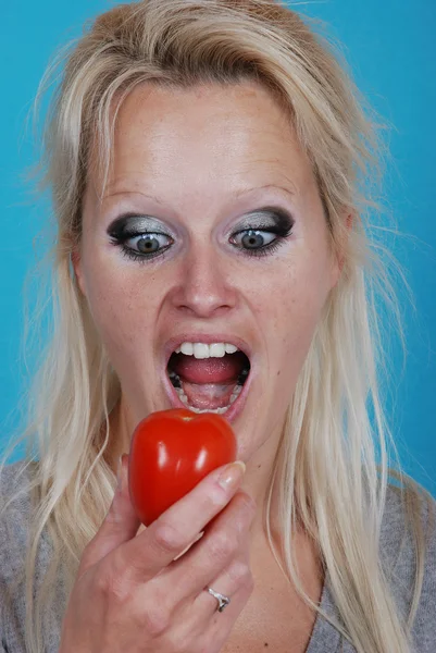 Blond womanl eating a tomato — Stock Photo, Image