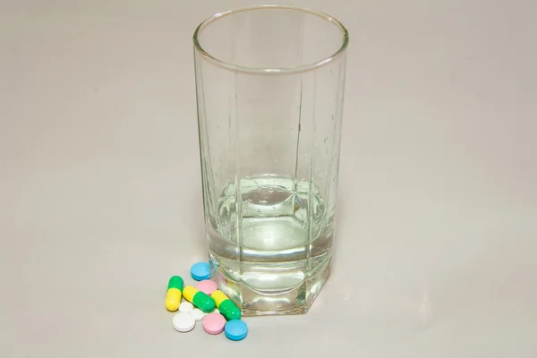 Multi-colored tablets with a glass of water — Stock Photo, Image
