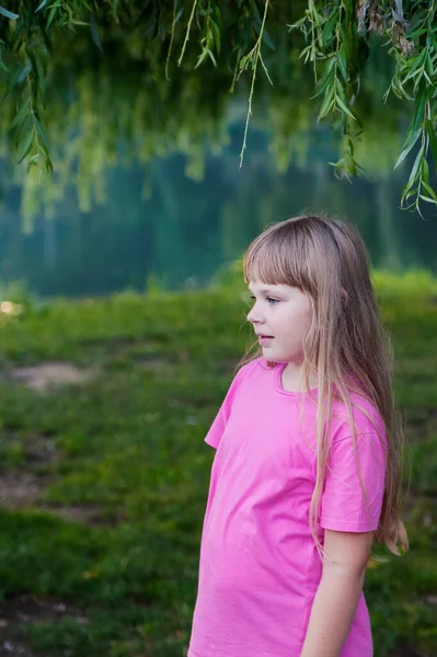 A girl in pink stands near a weeping willow by a pond. — Stock Photo, Image