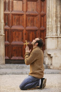 Man praying in front of the church holding a cross clipart