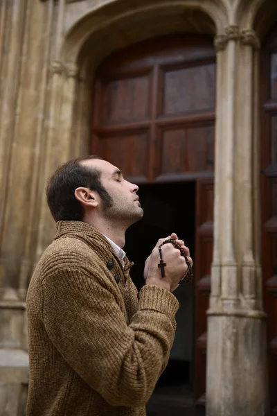 Hombre rezando en la iglesia sosteniendo cuentas de oración — Foto de Stock