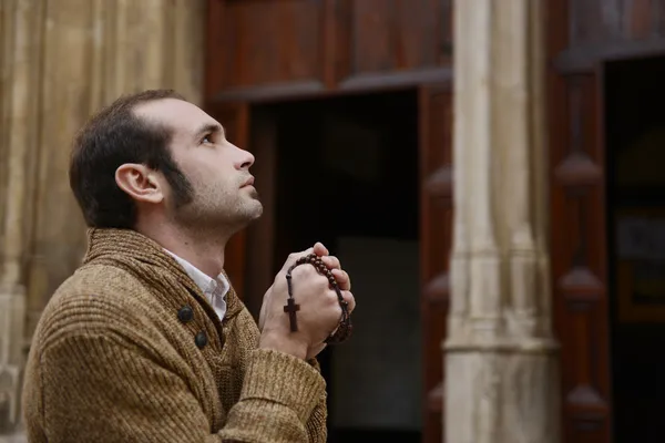 Hombre rezando en la iglesia sosteniendo cuentas de oración —  Fotos de Stock