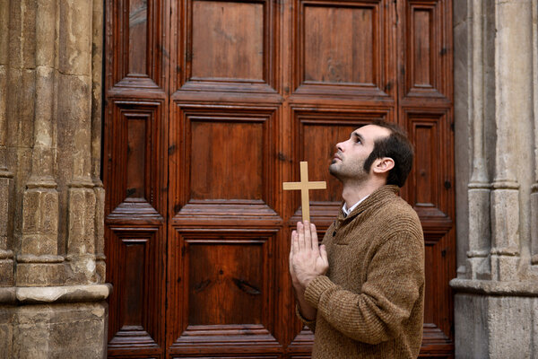 Man praying in front of the church holding a cross