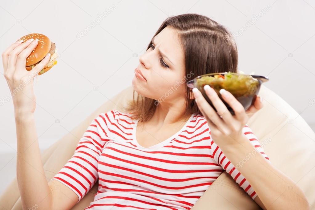 Slim woman choosing between a salad and hamburger