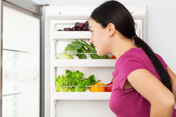 Junge Frau blickt in einen Kühlschrank — Stockfoto