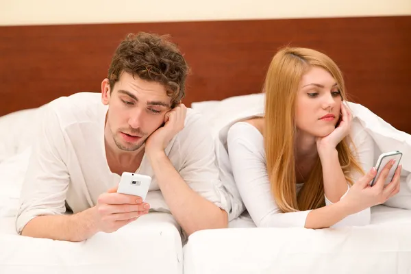 Fiatal pár okostelefonok az ágyban — Stock Fotó