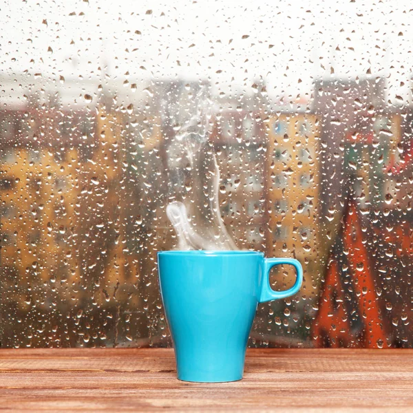Yağmurlu bir gün pencere arka plan üzerinde dumanı tüten kahve fincanı — Stok fotoğraf
