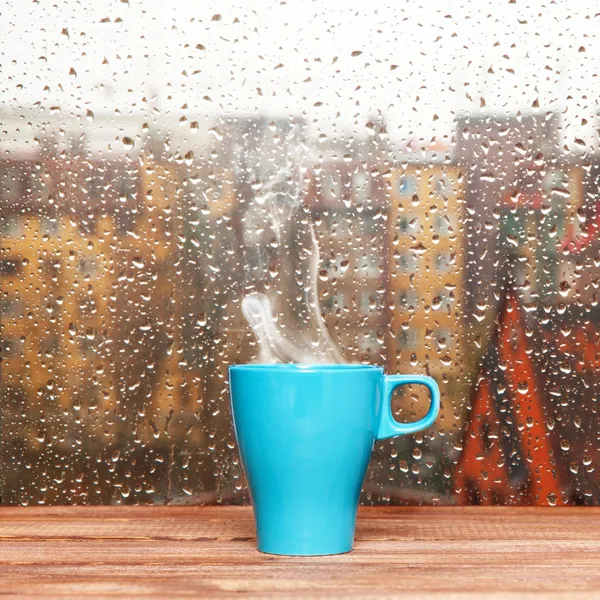 Taza de café al vapor en un fondo de ventana de día lluvioso — Foto de Stock