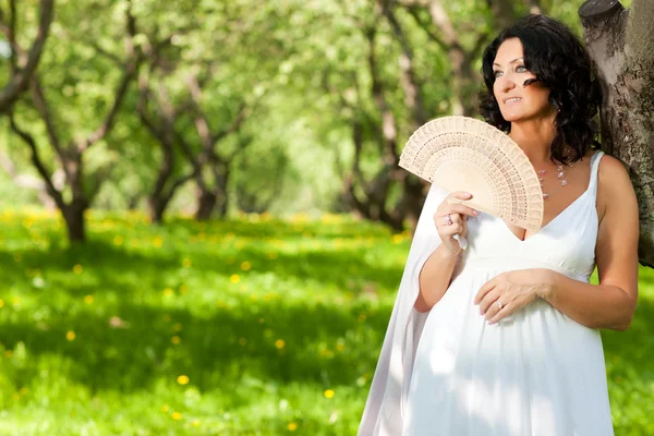 Женщина в парке держит вентилятор — стоковое фото