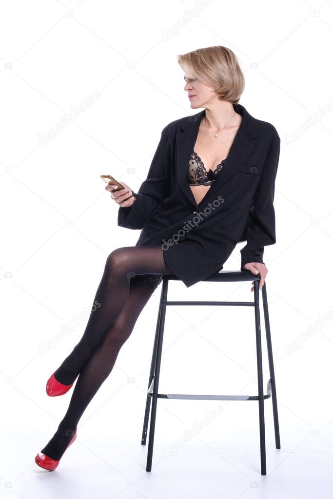 beautiful slender woman with a smartphone in her hands sits on a chair on a white background