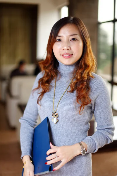 Улыбающаяся азиатская деловая женщина с папкой в офисе — стоковое фото