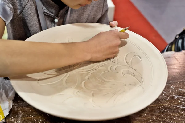 Handicraftsman engrave a white dish — Stock Photo, Image