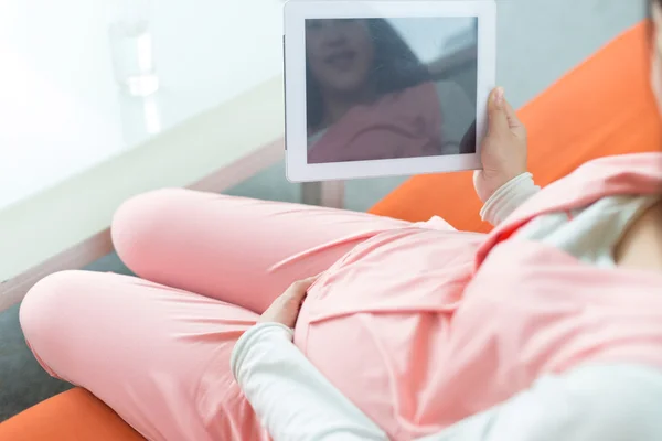 Glad gravid kvinna tittar på kameran, med hjälp av en digital tablet — Stockfoto