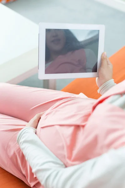 Glad gravid kvinna tittar på kameran, med hjälp av en digital tablet — Stockfoto