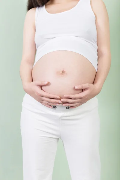 Беременная женщина держит руки на животе — стоковое фото