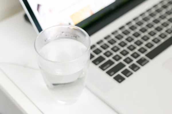 Laptop branco na mesa com vidro de água — Fotografia de Stock